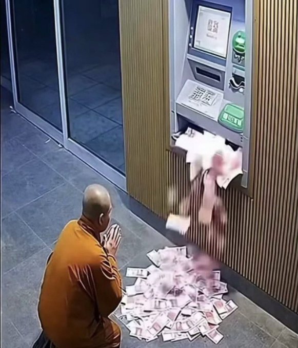 Surveillance camera footage shows a monk in orange robes kneeling in prayer in front of an ATM that has dispensed a large pile of cash onto the floor.