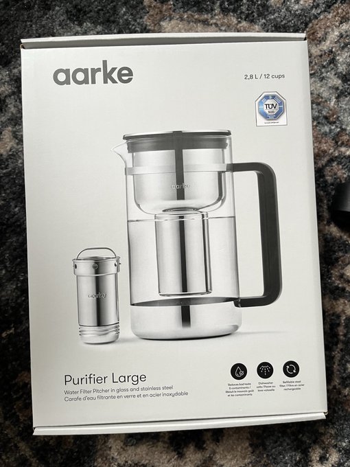 A product box for an 'aarke Purifier Large' water filter pitcher in glass and stainless steel, holding 2.8 L / 12 cups, with TÜV certification.