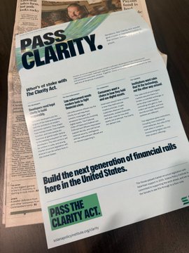 A newspaper page featuring a 'PASS CLARITY' advertisement calling for legislative action on the Clarity Act regarding digital assets.