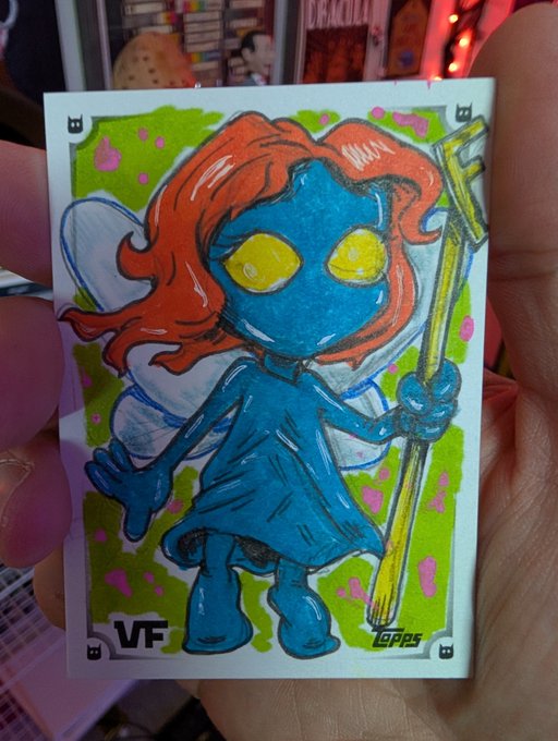 A hand-drawn sketch on a trading card showing a blue-skinned character with red hair holding a staff, marked with 'VF' and 'TOPPS'.
