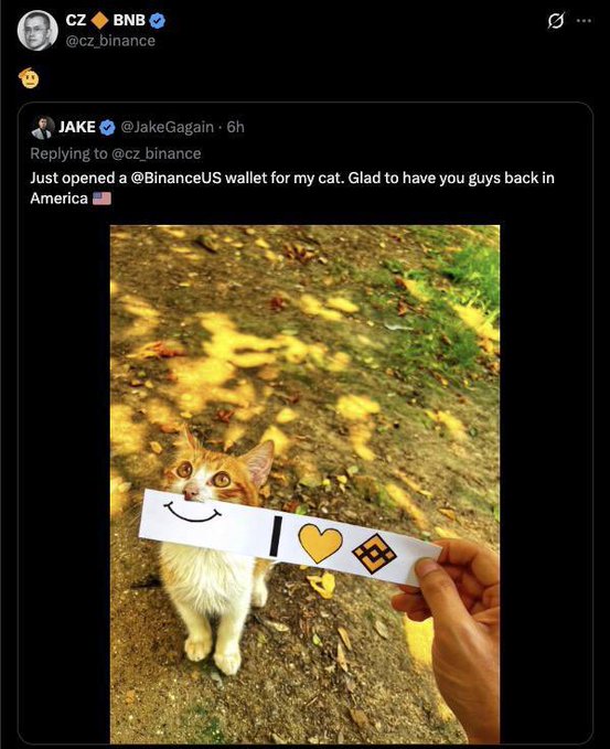 A screenshot of a Twitter post shows CZ from @cz_binance replying to JAKE (@JakeGagagain) who opened a @BinanceUS wallet for his cat, featuring a photo of an orange and white cat next to a sign reading smile, heart, and Binance logo.