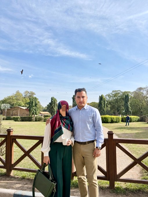 A couple stands together in a sunny park setting, smiling for a photo with a wooden fence and greenery in the background, as they send warm weekend wishes to their followers. The image complements the cheerful "Good Morning" greeting, inviting others to respond with a friendly "GM BACK."