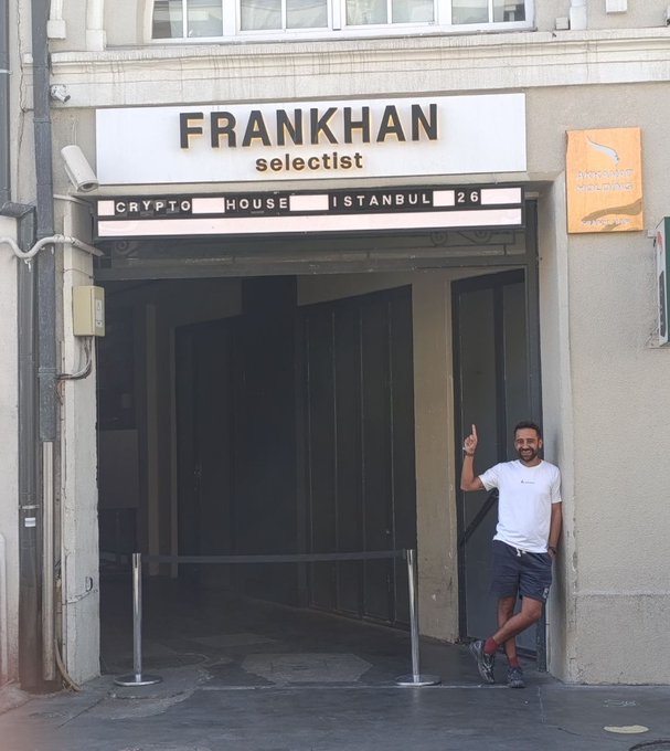 The image features a man standing outside of a building, possibly a store or an office, with his hand raised in a "thumbs up" gesture. The man appears to be posing for a photo, as he stands next to a sign that reads "FRANKHAN Selectist". The background includes a street scene and some buildings, indicating the location might be in a city setting. The post about GM Day seems unrelated to the main subject of the image, but it does provide context on when the photo was taken.