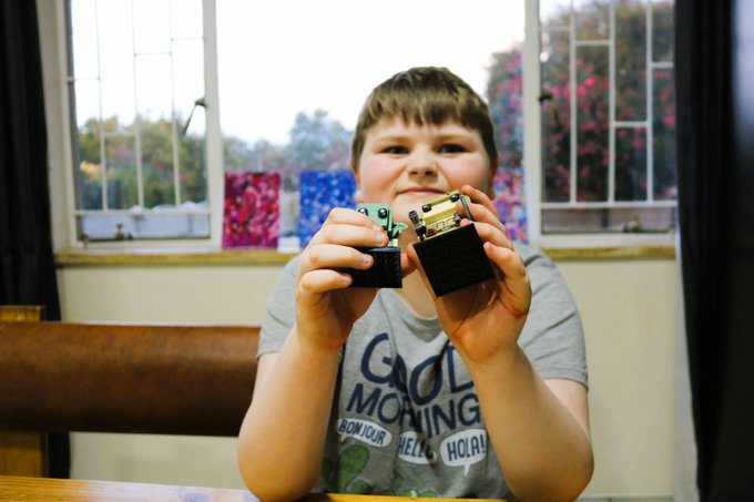 A smiling young boy wearing a "GOOD MORNING" t-shirt proudly holds up two lighters toward the camera.