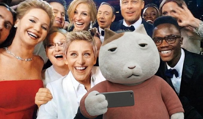 A cat character holds up a smartphone to take a group selfie with a star-studded cast of celebrities, including Jennifer Lawrence, Julia Roberts, Meryl Streep, George Clooney, Brad Pitt, and Kevin Hart, at what appears to be a formal awards ceremony.

The image relates to the post by depicting the cat mascot photo-bombing celebrity attendees, fitting the "$KET at the Top Cats 2026 Awards" theme.