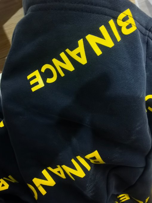 A close-up photo of a dark navy or black garment with 'BINANCE' printed in bold yellow letters, partially visible and folded.