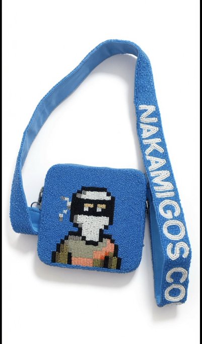 A blue fabric crossbody bag with a woven pixel-art character design and a strap reading 'NAKAMIGOS CO'.