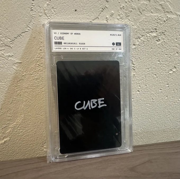 A graded trading card or collectible slabbed in a clear protective case, labeled 'VV / ECONOMY OF WORDS' with 'CUBE' as the title and 'ONE OF ONE' notation, showing a black card with 'CUBE' handwritten in white.