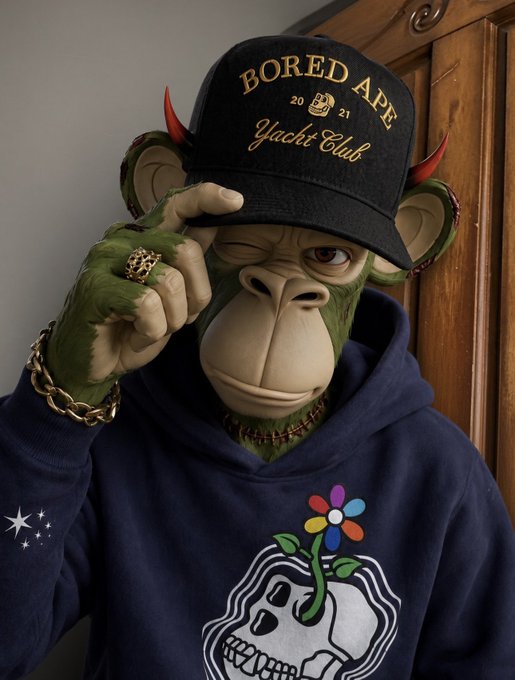 A 3D-rendered anthropomorphic ape character wearing a black "Bored Ape Yacht Club 2021" cap, a navy hoodie with a skull-flower graphic, and gold chain jewelry, tipping its hat.