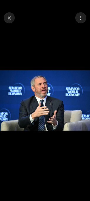 A man in a dark suit and striped tie speaks while gesturing with his hands at the 'SEMAFOR WORLD ECONOMY' summit.