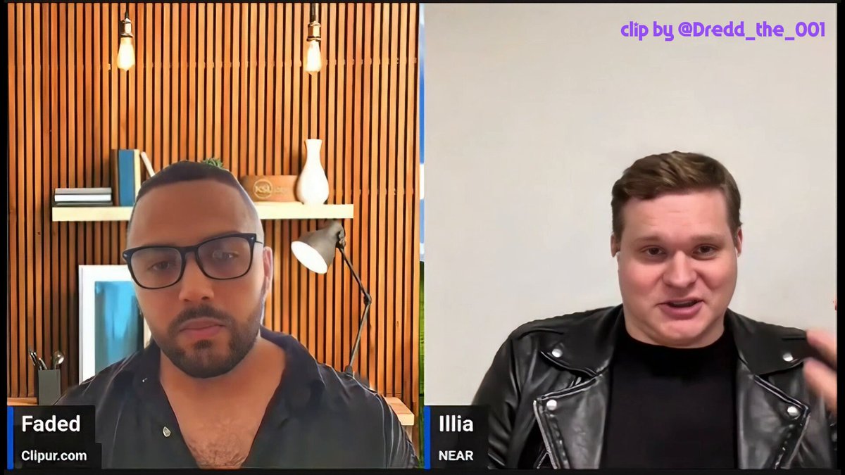 The image shows two men sitting across from each other, with a computer screen displaying their conversation. One man wears glasses and has a beard, while the other man is wearing a leather jacket. They appear to be discussing something related to Bitcoin or AI, as indicated by the caption provided in the image.