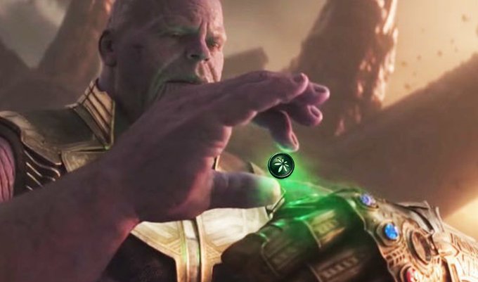 A still of the character Thanos from a Marvel film, holding up a glowing green Time Stone from the Infinity Gauntlet.
