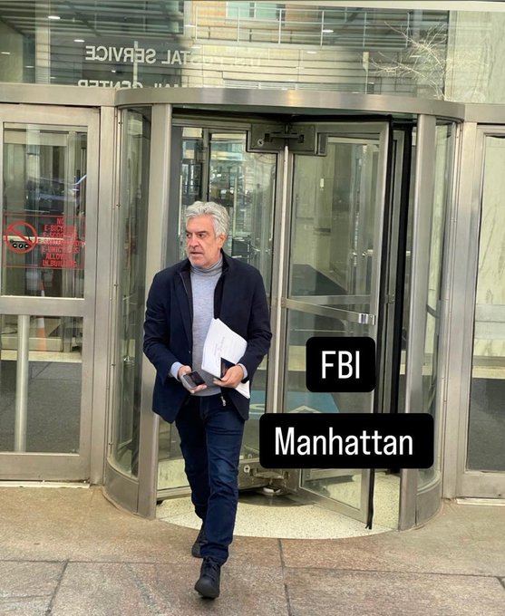 A man with white hair and glasses exits a revolving door while holding papers, with overlay text reading 'FBI Manhattan'.