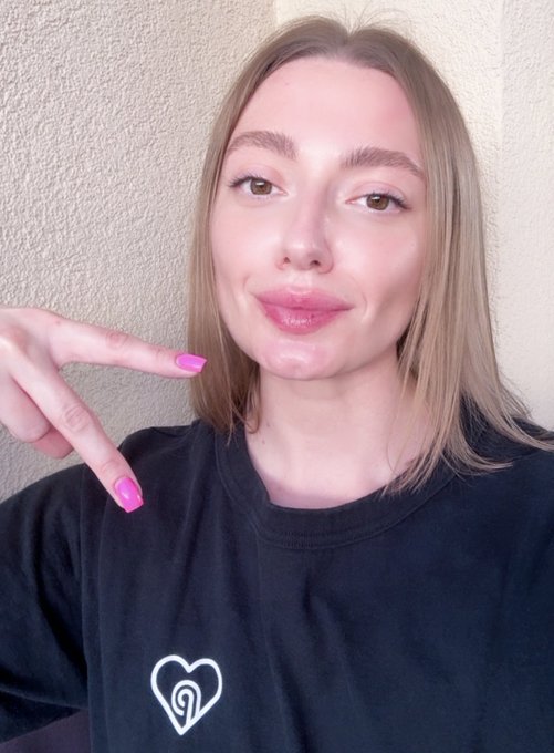 A woman with pink nails points toward her face while wearing a black shirt featuring a heart logo with a stylized "P" inside, matching the Pyth Network branding referenced in the celebratory Pythday post.