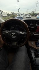 A point-of-view photograph from inside a Lexus, looking past the steering wheel toward other cars on a road.