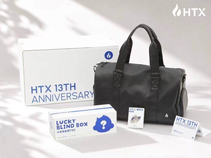 A black duffel bag and a "Lucky Blind Box" are displayed alongside an "HTX 13TH ANNIVERSARY" branded box, marking the arrival of HTX (formerly Huobi)'s 13th anniversary merchandise.