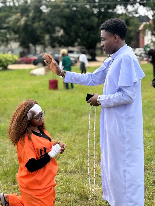 A kneeling woman in an orange jumpsuit with bandaged head and hands receives a blessing from a man in white robes holding prayer beads, as the ritual scene evokes a solemn, "blessed" morning mood—perfectly fitting a post asking followers to share one word describing how they feel.