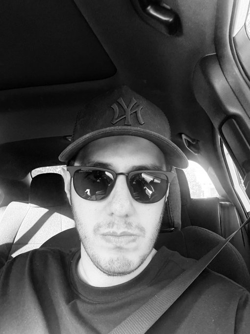 A man wearing a New York Yankees cap and sunglasses takes a black-and-white selfie in his car, fitting the late Friday grind vibe as he heads to work at Quip Network.