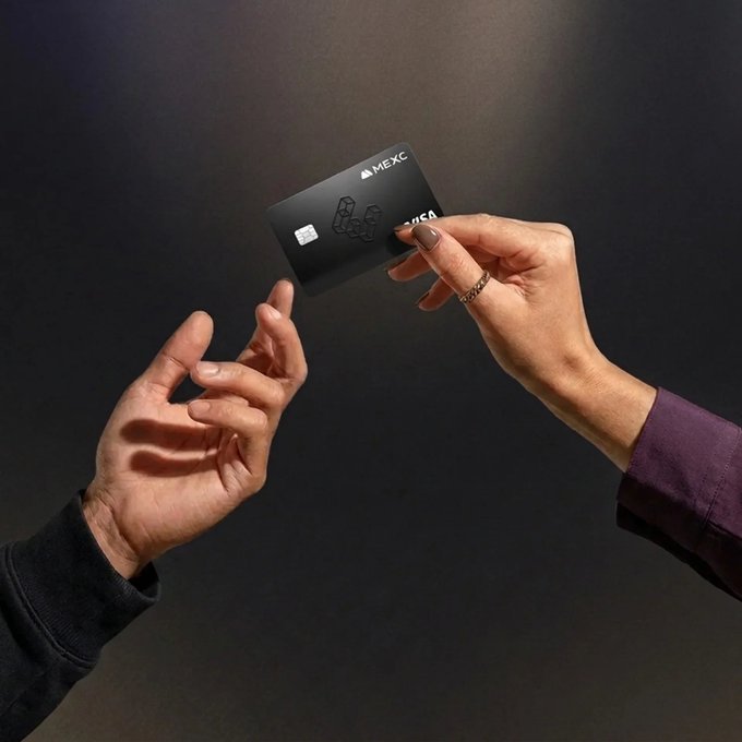 Two hands exchanging a black MEXC credit/debit card against a dark background.