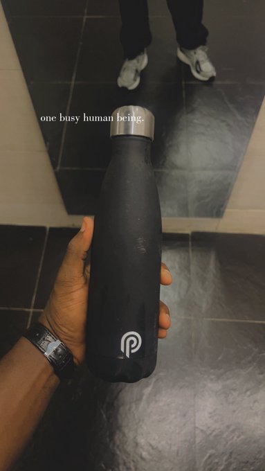 A hand holds a black insulated water bottle with a silver cap featuring a stylized 'P' logo, photographed in a mirror with the caption 'one busy human being.'