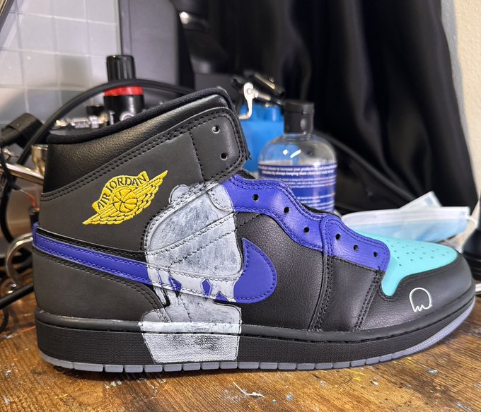 A custom black Air Jordan 1 high-top sneaker featuring a blue Nike swoosh, light blue toe accent, and a hand-painted melted candle design across the side panel, displayed on a wooden surface alongside shoe care products. The post showcases this artistic custom design as part of a creative NFT collaboration, reflecting the MetaVixens brand's blend of streetwear and digital art.