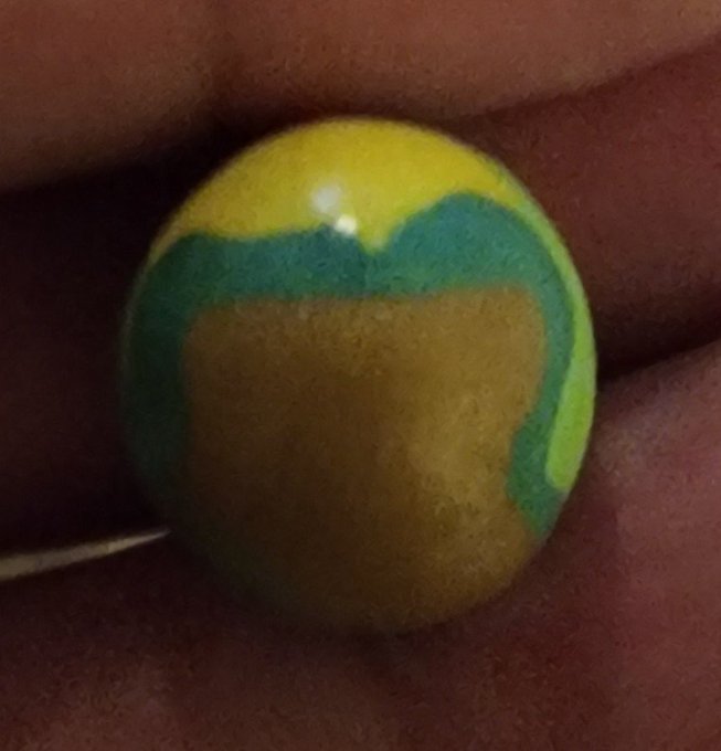 A close-up of a person's palm holding a yellow marble or bead with a green band around it.