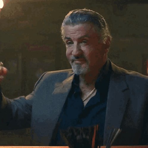 The image features a man wearing a suit, sitting at a table with his arm outstretched. The background appears dark, which contrasts with the bright light from above that illuminates the scene. There are also some objects present in the room, such as a cup and a bowl on the table. The post includes text about burning 4.7mil Hefe in the @AvaxHefe app to show support for @rainsright and to express his convictions.