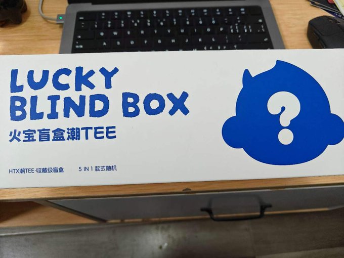 The image features a white box with blue text that reads "Lucky Blind Box" along with an image of a cartoon character, likely a baby or a child's face. The box appears to be from a company named Huobi Global, as indicated by the "@HTX_Molly @HuobiGlobal" in the caption.