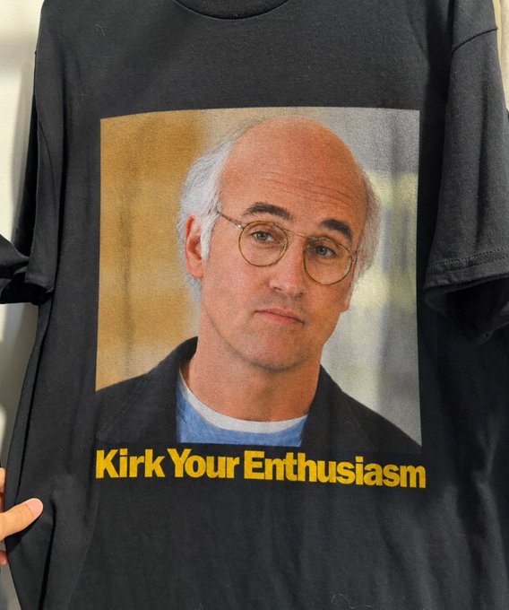 A black t-shirt features a portrait of a bald man with glasses, with yellow text reading 'Kirk Your Enthusiasm'—a play on the Seinfeld catchphrase.