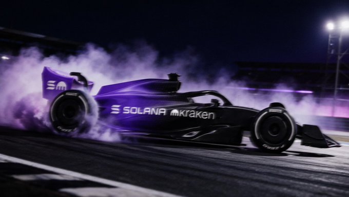 A Formula 1 race car performs a dramatic burnout at night, with purple smoke billowing from its tires as it sits on a race track. The vehicle prominently displays sponsor logos for "SOLANA" and "Kraken," along with the number "30" on the rear wing.