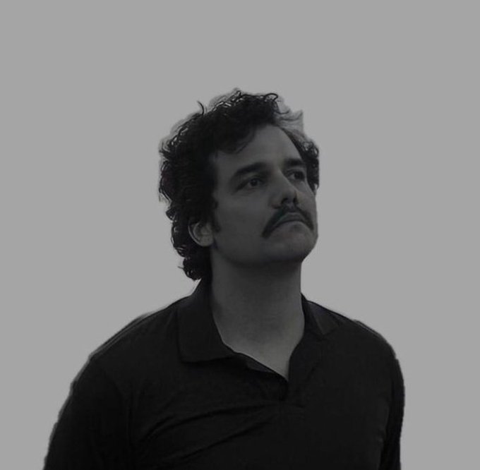 The image features a man with curly hair wearing a black shirt, looking up at something above his head. The photo has been edited or altered to appear as a black and white image, giving it an artistic touch. The caption below the image reads "thinking about the guy who told me Bitcoin was a scam in 2019." This suggests that the man might be contemplating the story behind the image or pondering the history of Bitcoin.