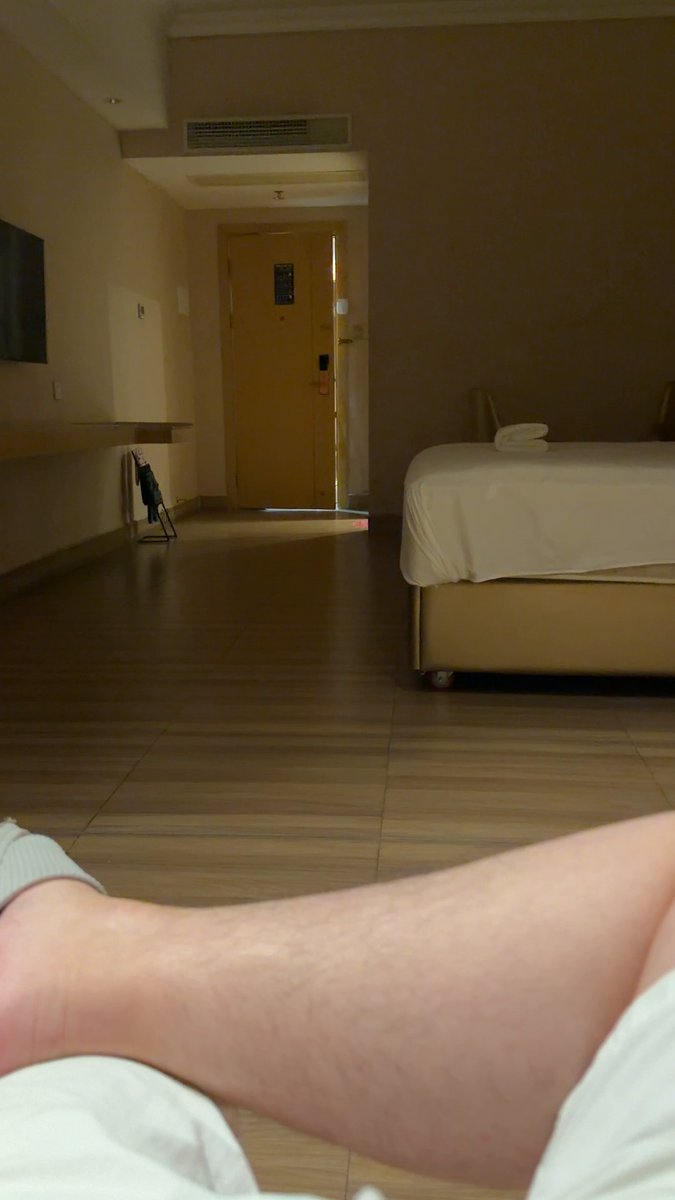 The image shows a person's leg resting on a bed, with their foot visible underneath them. The room appears to be a hotel room or bedroom, as indicated by the presence of a bed and a door leading out to another area within the building. The photo is taken from an angle that looks down upon the person's leg, giving it a unique perspective. The image also contains text that reads "Went out to play for a week Perfectly dodged the extreme market One more night of play at the end Tomorrow go all-in on BSC". This message seems to be related to the person's decision to stay in and relax instead of going out, possibly due to unfavorable weather conditions or other circumstances.