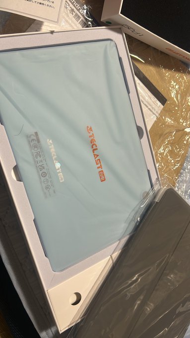 A photo of a Teclast tablet in its white retail packaging, featuring a light blue protective sleeve with the Teclast logo and product specifications sticker visible.