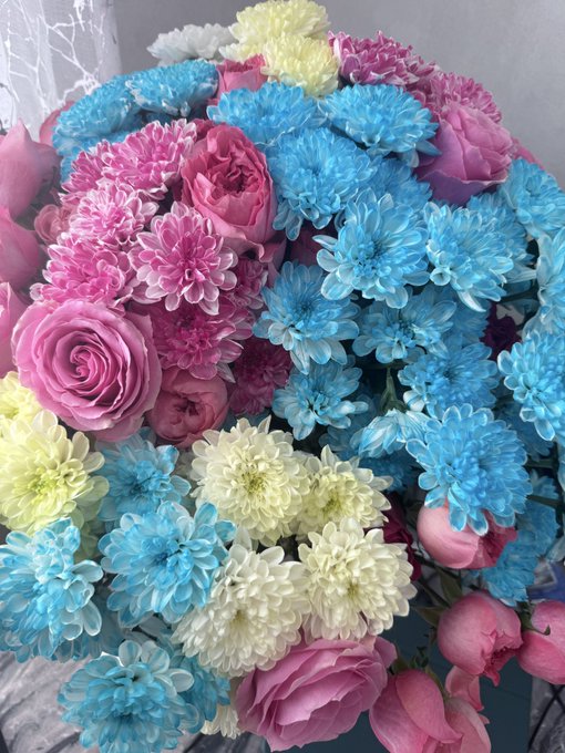 A vibrant bouquet of dyed chrysanthemums and roses in shades of pink, blue, yellow, and cream fills the frame.