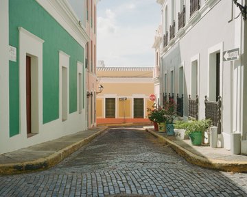 A picturesque cobblestone street corner with brightly colored buildings in shades of green, yellow, and white.