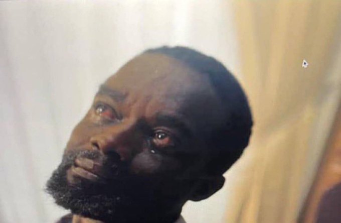 A close-up still from a film showing a Black man with a beard looking upward with tear-filled eyes, appearing emotional against a blurred background.
