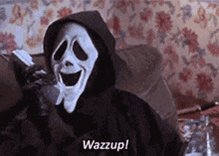 The image features a person wearing a scary or evil-looking mask, possibly a skeleton or a monster mask from the movie "Scary Movie", sitting on a couch with their arms outstretched as if they are waving at someone. The text below the image reads "Wazzup!".