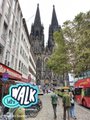 A street view showing a large Gothic cathedral in the background with crowds of people and shops in the foreground.