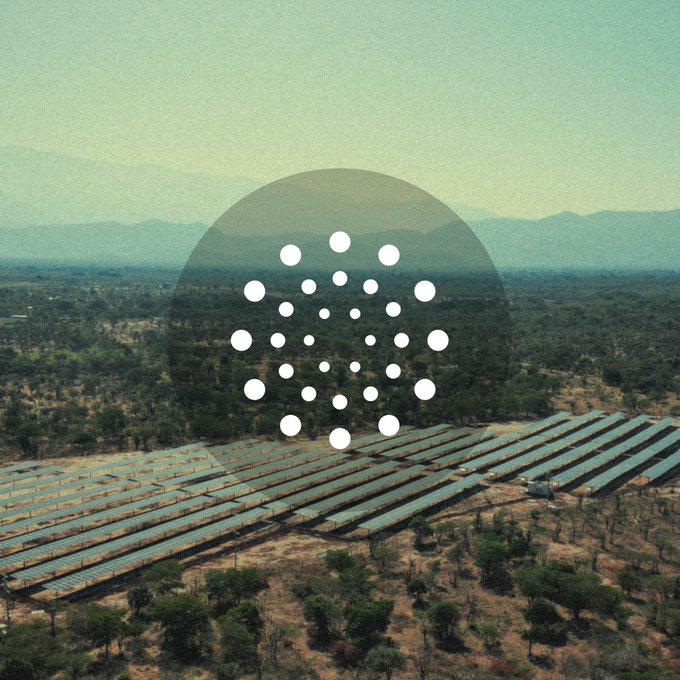 Aerial view of a solar panel farm with the Cardano (ADA) logo overlaid in the center.