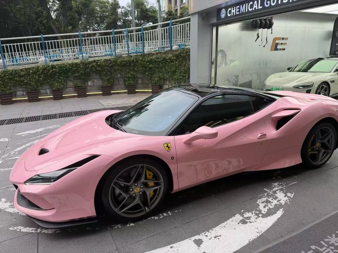 A pink Ferrari F8 sports car parked on a street in front of a building labeled 'CHEMICAL GUYS'.