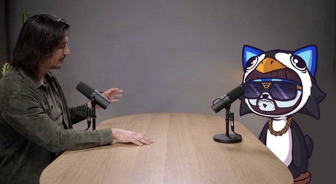 A photoshopped image showing a man with dark hair sitting at a podcast table across from an edited cartoon penguin character wearing sunglasses and a gold chain.
