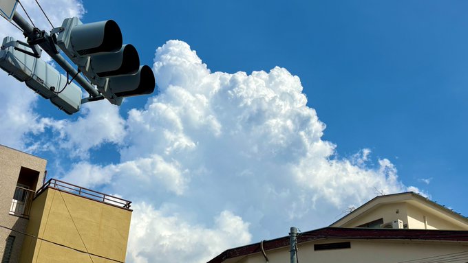 Traffic lights and rooftop antennas frame a dramatic, towering cumulus cloud against a vivid blue sky, capturing the iconic summer sky over Tokyo.