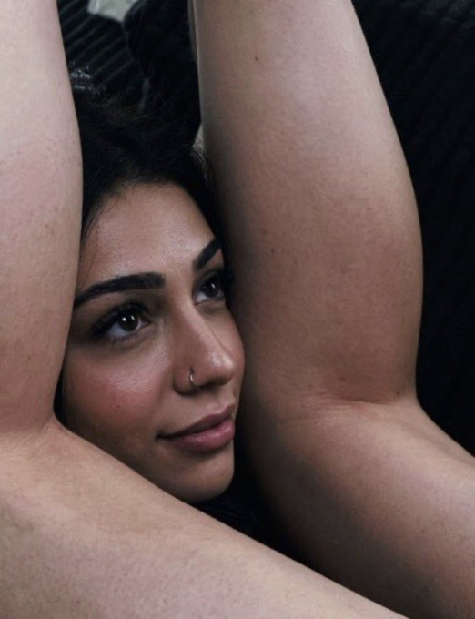 A woman with her arms raised frames her face with a subtle, unimpressed expression, her eyes gazing sideways in quiet judgment. The image pairs with the caption to capture the silent, skeptical look someone gives when their romantic interest reveals their "investment portfolio" is built entirely on a meme cryptocurrency.