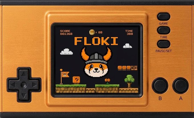 An orange handheld gaming device displays a pixelated Floki-themed game featuring a viking-helmeted Shiba Inu character, with "SCORE 001368," "x 88," and "TIME 388" visible on screen alongside a "? block," flag, and platformer terrain. The "Press B to build" prompt relates to the prominent B button on the console's control pad, which would be used to construct within the game's block-building platformer environment.