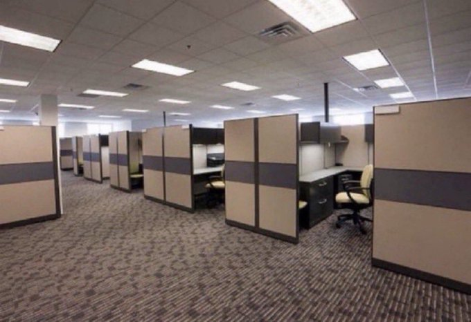 The image shows an empty corporate office floor with rows of vacant cubicles, beige partitions, and unoccupied desks. This relates to the post's warning by visually representing the consequence of not securing employment—a barren, lifeless workspace filled with unused workstations rather than engaged employees.