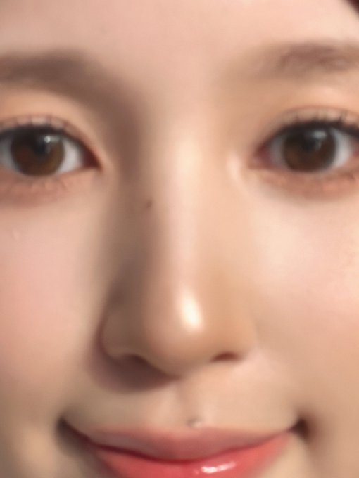 A close-up, soft-focus photograph of a person's face, highlighting their eyes, nose, and glossy lips with a slight smile.