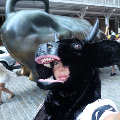 A person poses in front of a bronze bull statue while wearing a black bull head mask with an oversized open mouth showing teeth, cleverly mirroring the iconic Charging Bull in the background to reinforce the "Bull stays on $ANSEM" sentiment of unwavering bullish confidence.