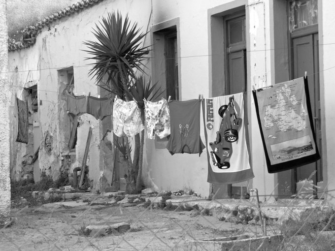 A black and white photograph shows laundry hanging on a clothesline in a rustic courtyard, with a yucca plant and stone walls in the background.
