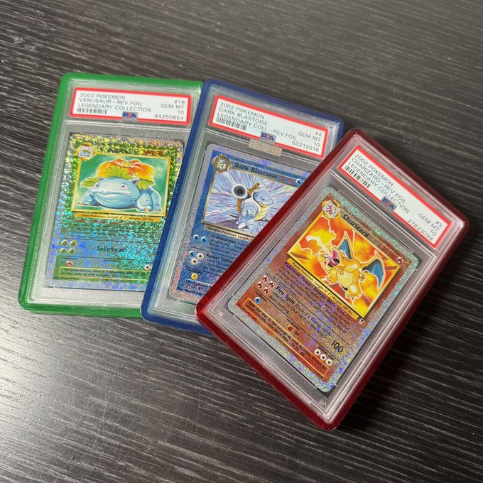 Three PSA-graded Pokémon cards are displayed in green, blue, and red graded cases: Venusaur (2002 Pokémon, #18), Dark Blastoise (2002 Pokémon, #7), and Charizard (2002 Pokémon, #2).