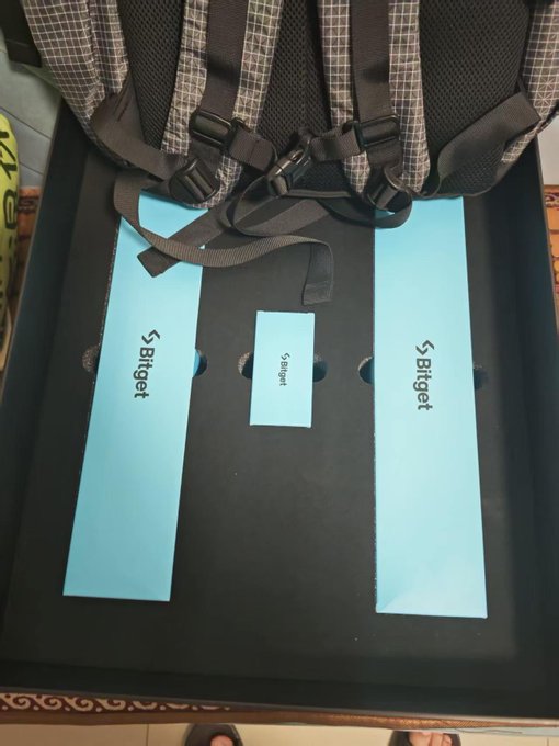An overhead view showing the back panel of a chair with three light blue 'Biget' branded labels/stickers placed on it, with backpack straps visible at the top.